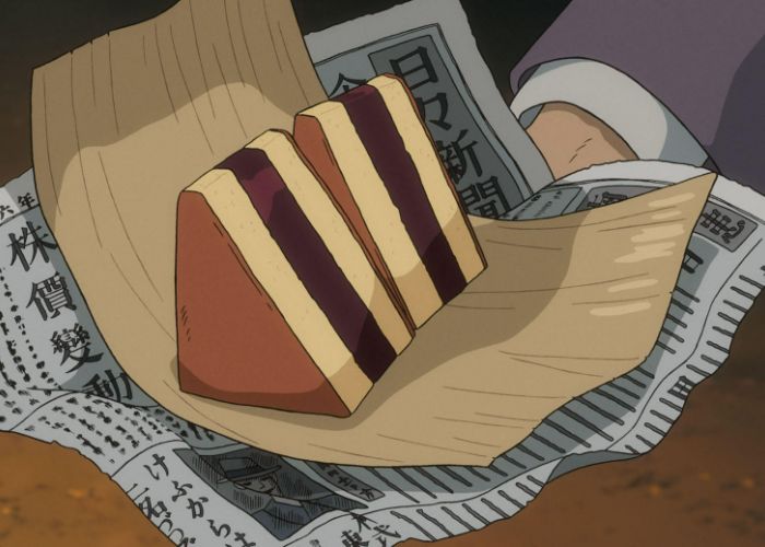 Two slices of Siberia cake are wrapped in newspaper, showing red bean paste sandwiched between two slices of castella cake.